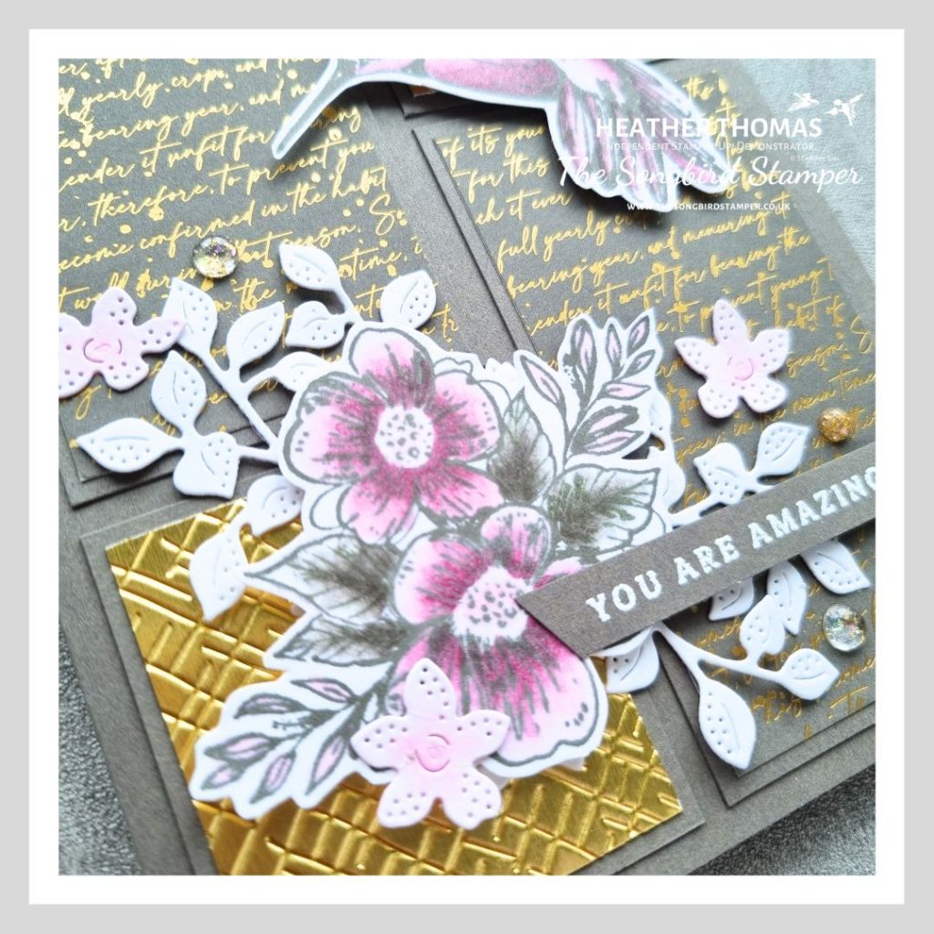 A close up of a gold and grey panelled handmade card with a pop of color in pink, with a hummingbird and a floral and leaf image.