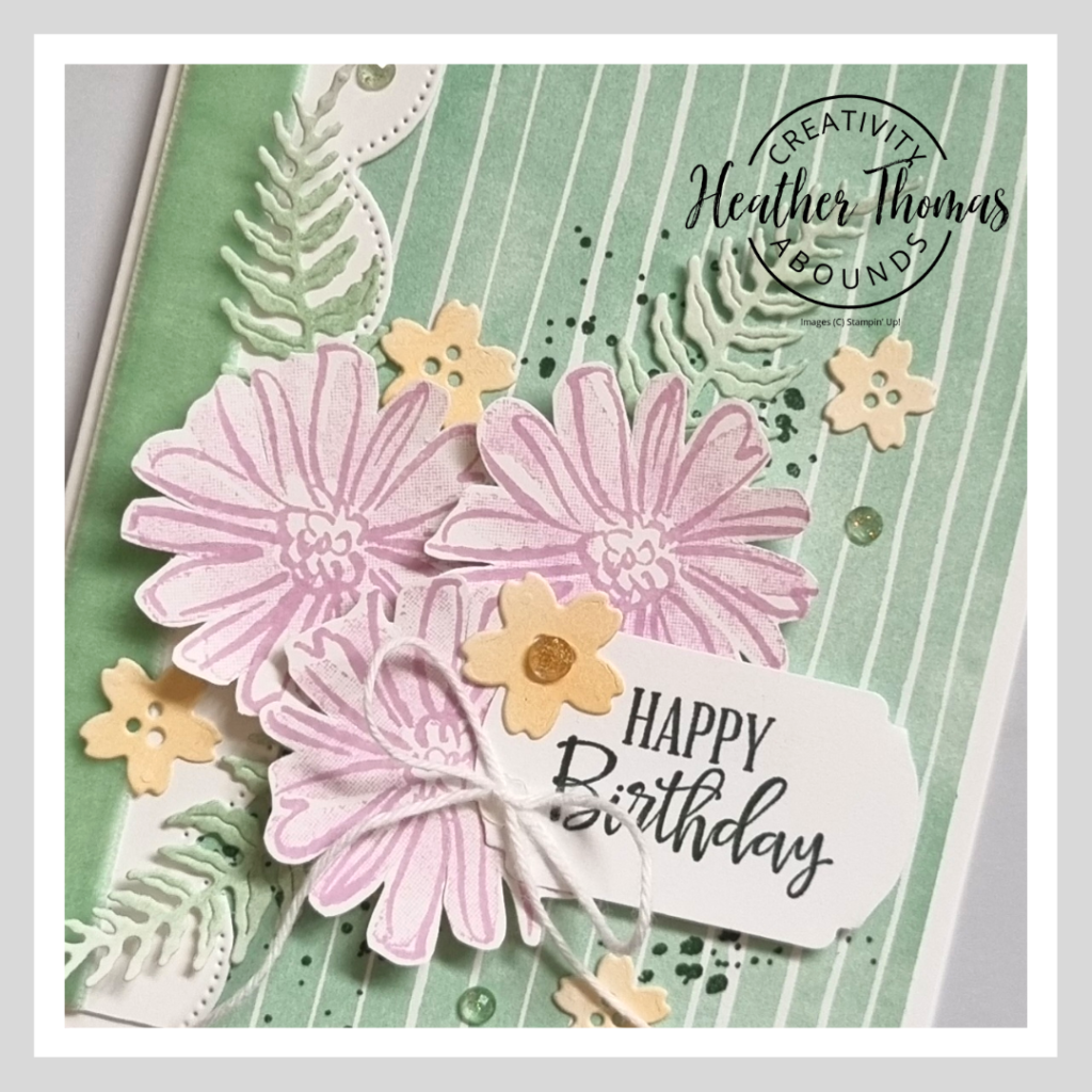 A close up of a handmade fun and fresh birthday card in green, purple and orange with three flowers and some leaves.