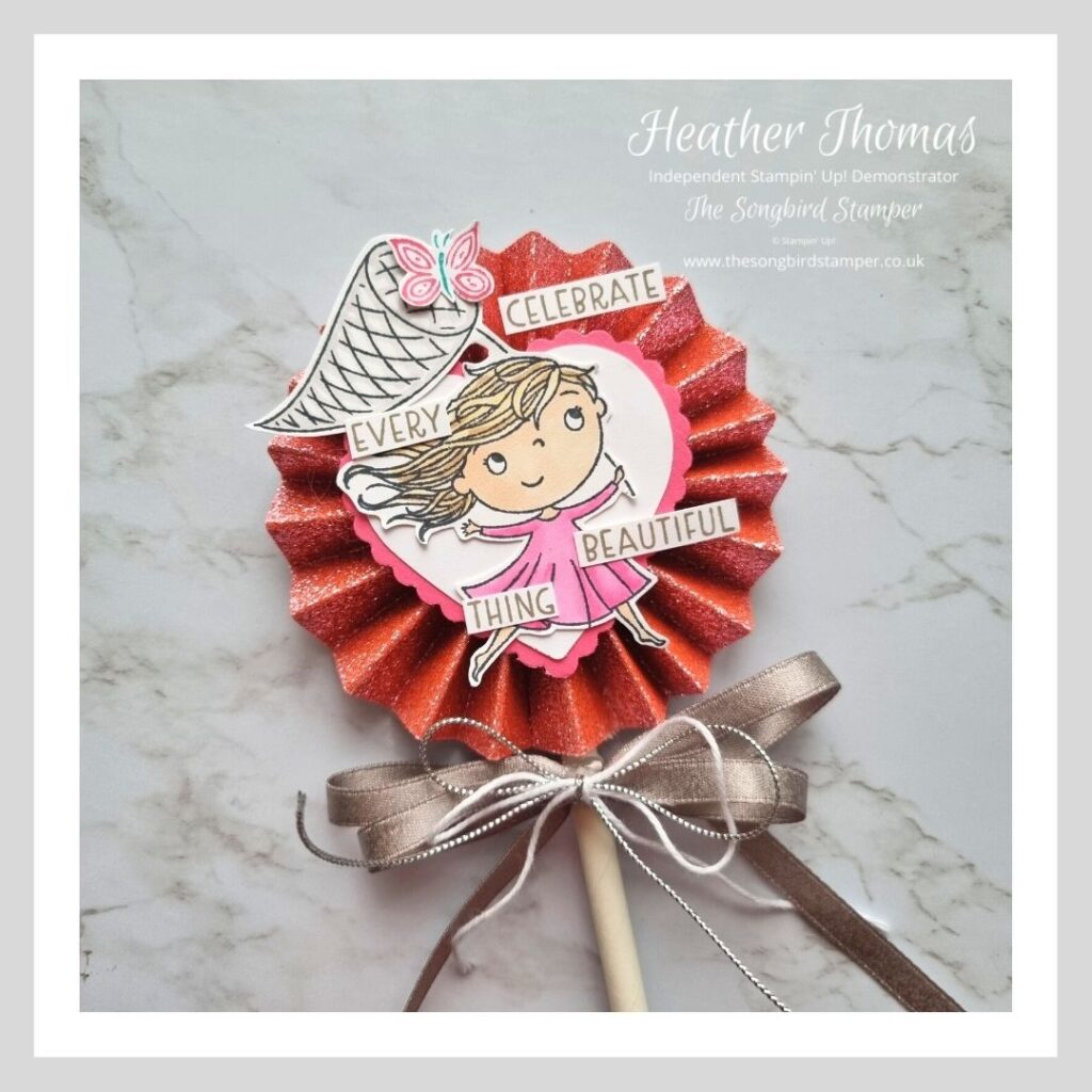 A photo of a paper rosette with a little girl catching butterflies, in pinks and greys. 