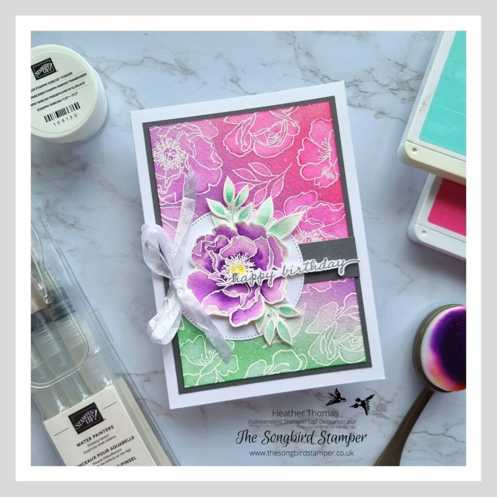 a flowery card in purple, pink and teal, with a faux bleach technique background and a focal point of a watercoloured flower.