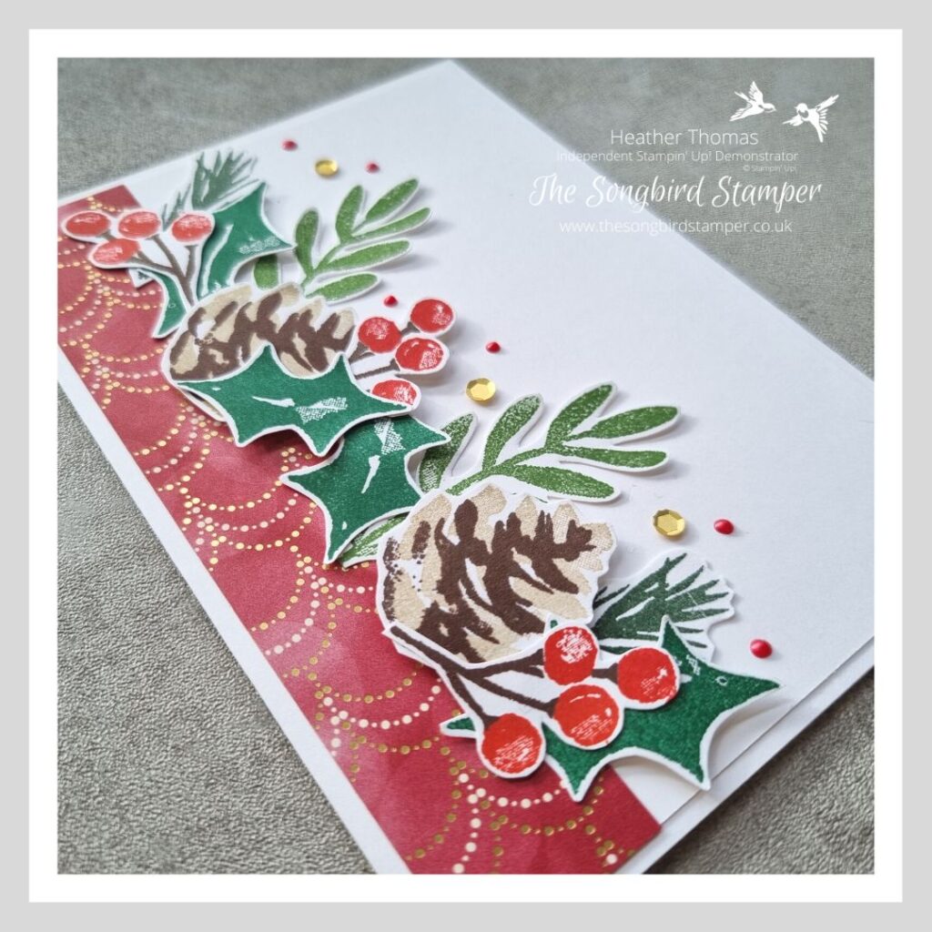 A Christmas card in red, green and gold, with pine cones, leaves and berries.