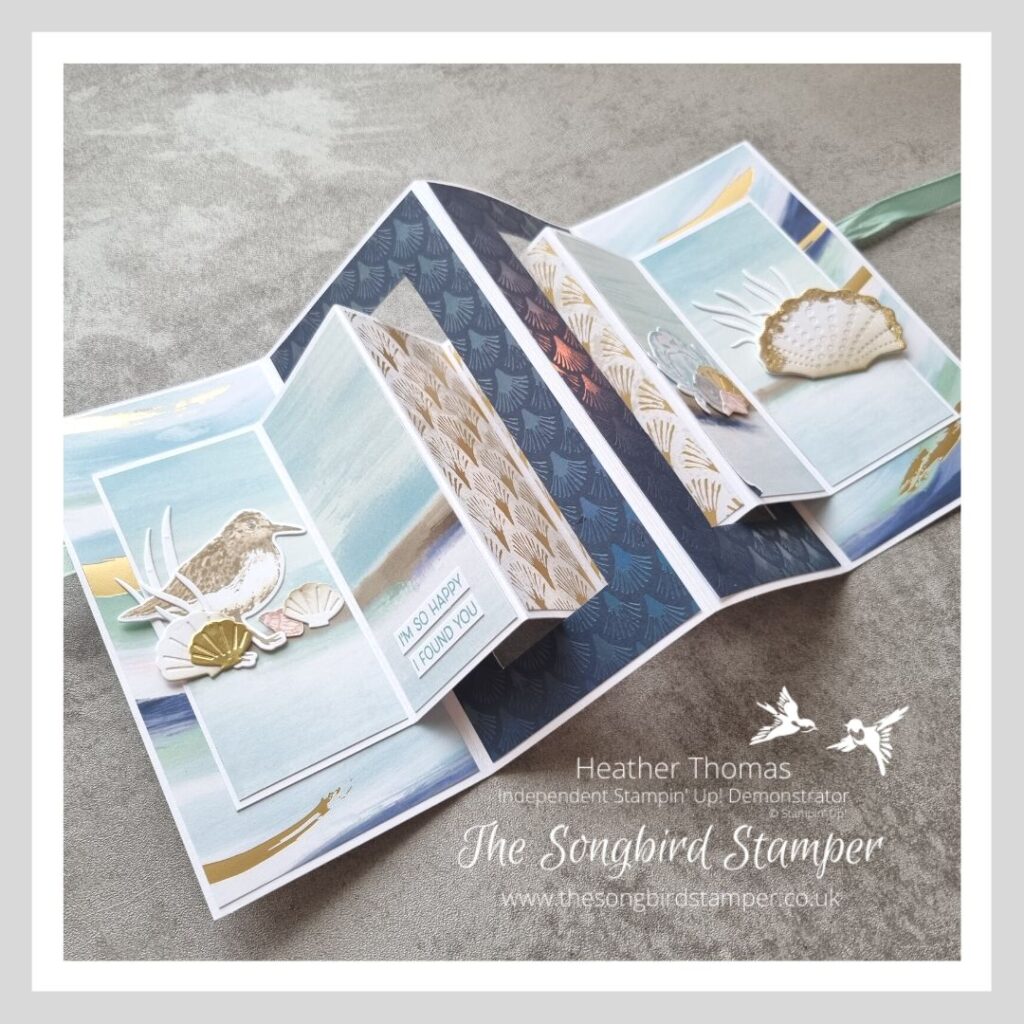 The inside of an accordion fold card, with blue and gold papers, wading birds and shells.