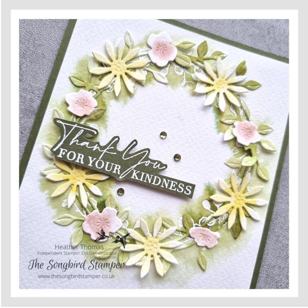 A handmade card in greens, pinks and yellows, with a wreath of flowers using the emboss resist technique