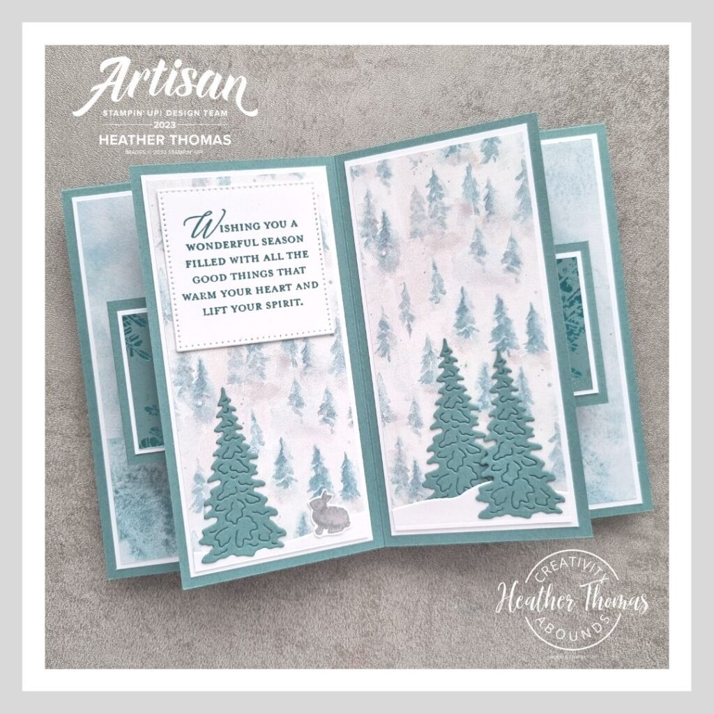 A suspended book fold card in an aqua colour with trees and a christmas sentiment.