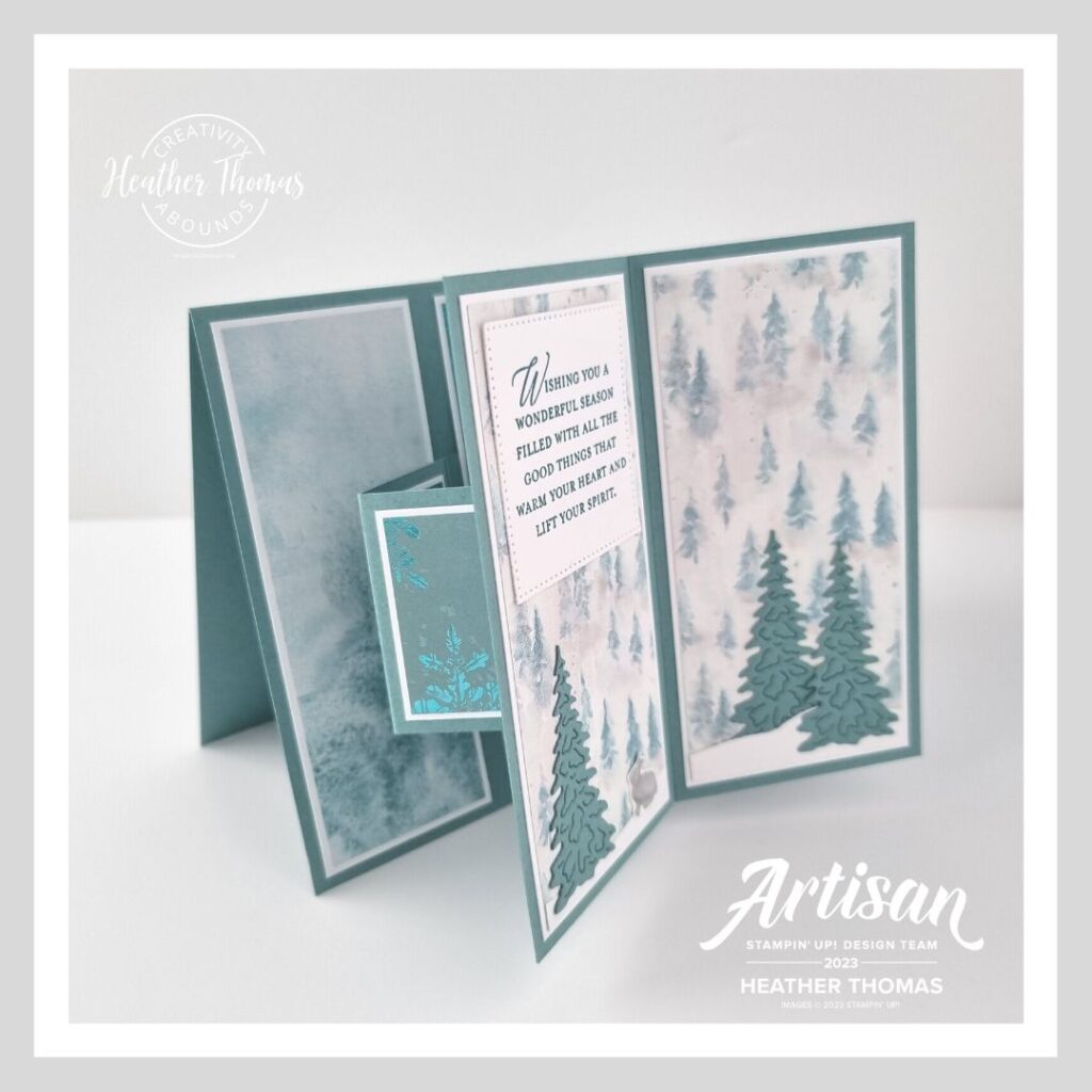A side view of a suspended book fold card in an aqua colour with trees and a christmas sentiment.
