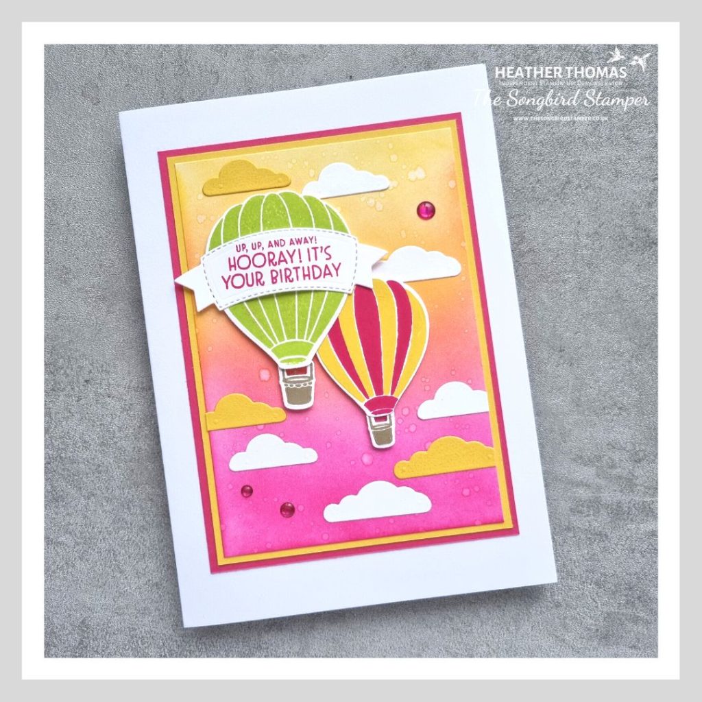 A handmade card in yellow, pink and green with two hot air balloons over an ink blended sunset sky
