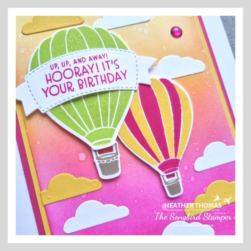 A close up of a handmade card in yellow, pink and green with two hot air balloons over an ink blended sunset sky