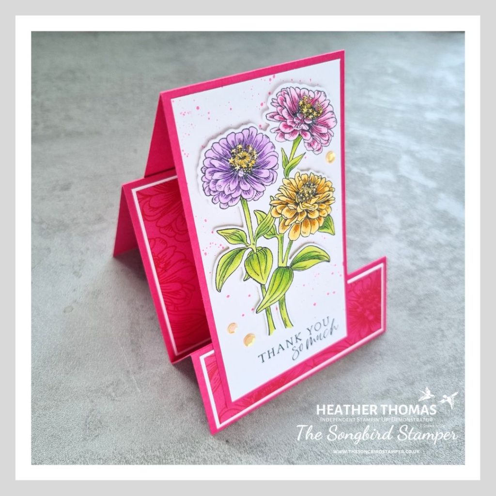 A faux stepper card in pink, with flowering zinnias coloured in with green, yellow, purple and pink