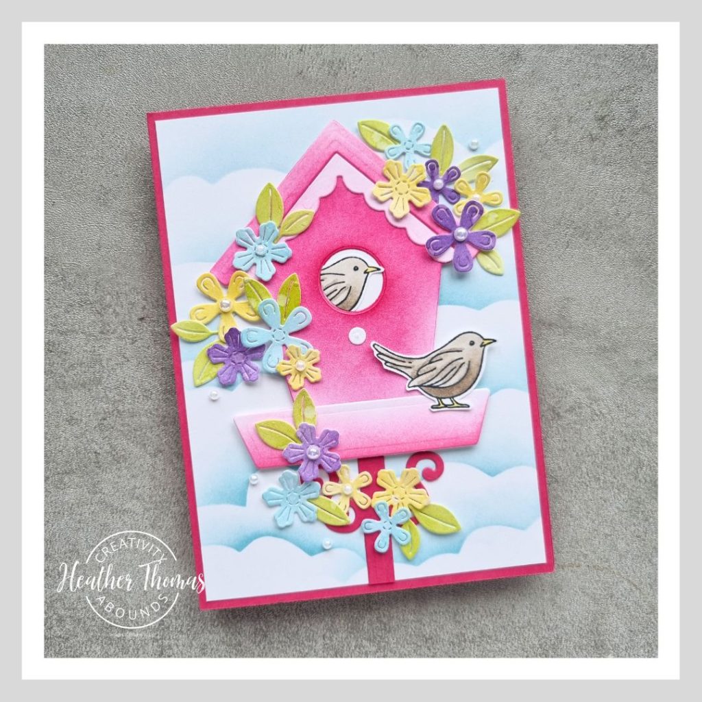 A fun and vibrant handmade card with a pink birdhouse, two cute brown birds and a whole heap of purple, blue and yellow flowers decorating it. Made with the Country Birdhouse bundle from Stampin' Up!