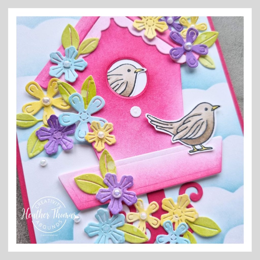 A fun and vibrant handmade card with a pink birdhouse, two cute brown birds and a whole heap of purple, blue and yellow flowers decorating it. Made with the Country Birdhouse bundle from Stampin' Up!